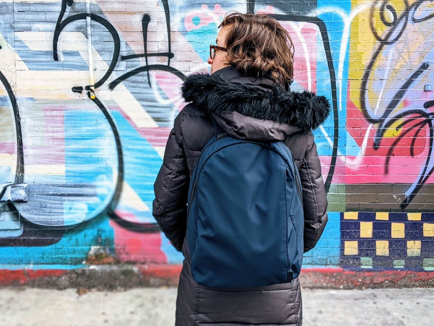 Woman wearing the Away travel daypack in blue against a colorful wall